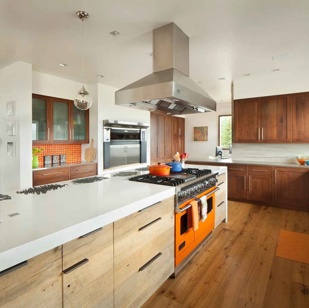 Ejemplo de cocina rústica con armarios estilo shaker, puertas de armario de madera oscura, electrodomésticos de colores, suelo de madera en tonos medios y una isla