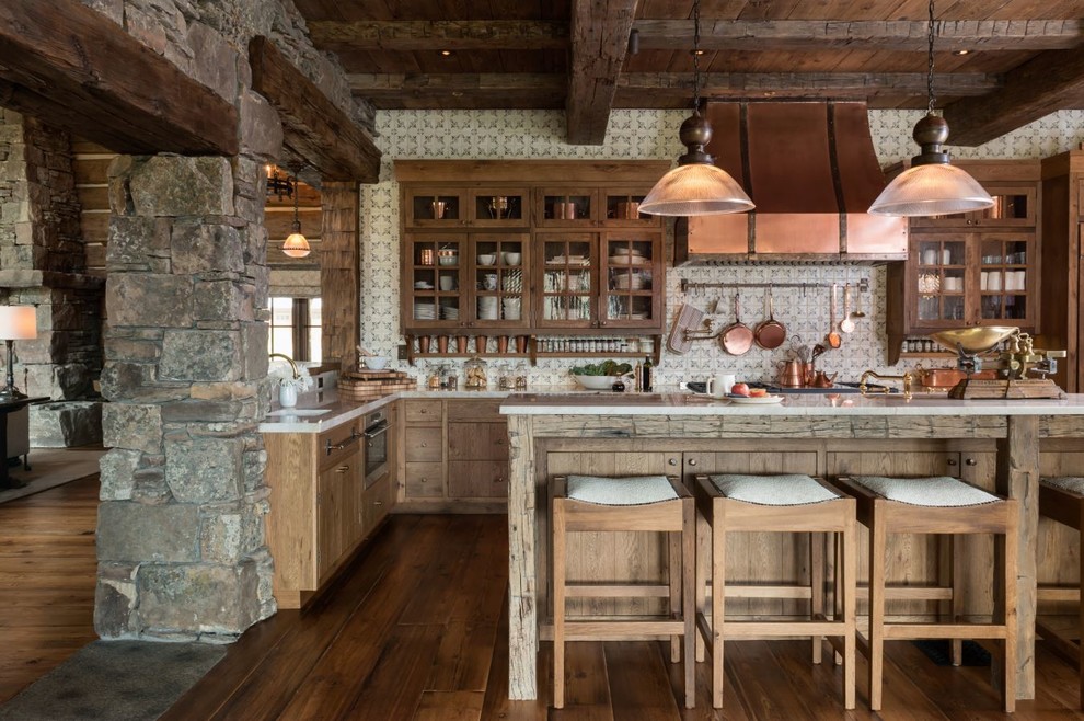 Inredning av ett rustikt l-kök, med en undermonterad diskho, skåp i mellenmörkt trä, vitt stänkskydd, mörkt trägolv och en köksö