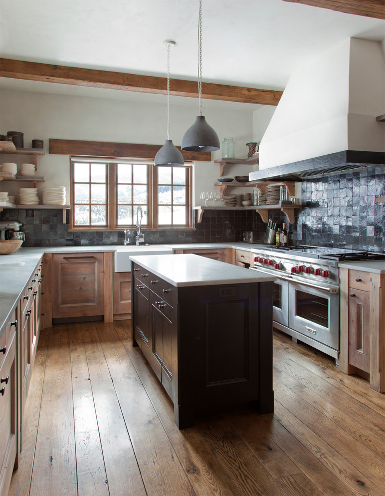 Cette image montre une cuisine chalet en U et bois brun avec un évier de ferme, un placard à porte shaker, une crédence noire, un électroménager en acier inoxydable, un sol en bois brun et îlot.