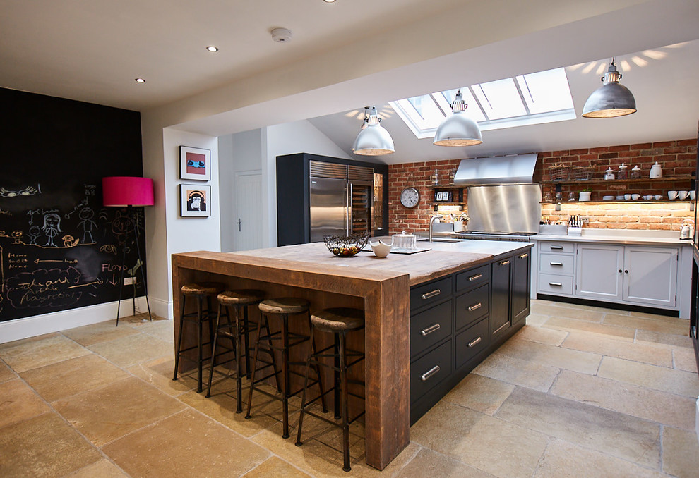 Photo of a rustic u-shaped kitchen in Other with a submerged sink, shaker cabinets, black cabinets, wood worktops, red splashback, brick splashback, stainless steel appliances, limestone flooring, an island, beige floors and brown worktops.