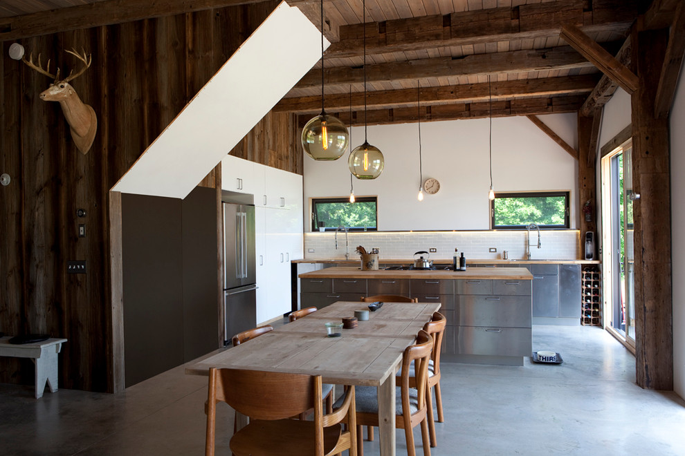 Rustik inredning av ett kök och matrum, med släta luckor, skåp i rostfritt stål, träbänkskiva, vitt stänkskydd och rostfria vitvaror