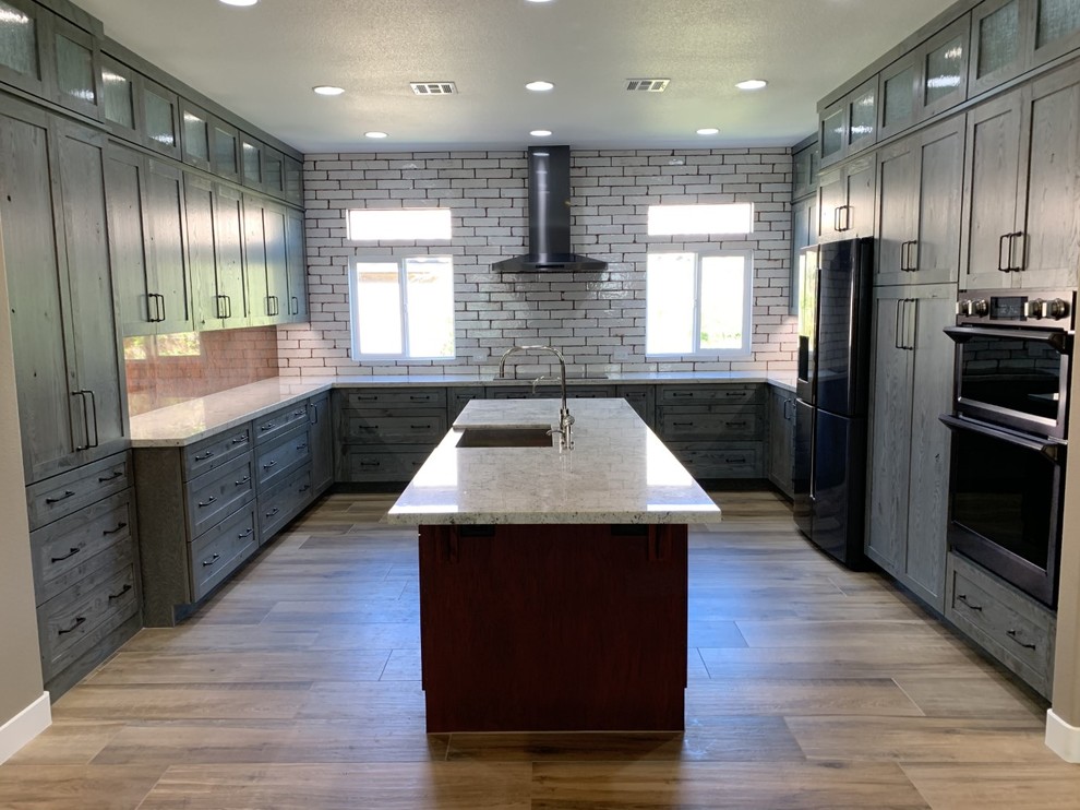 Kitchen - large rustic u-shaped medium tone wood floor and brown floor kitchen idea in Las Vegas with shaker cabinets, an island, a farmhouse sink, gray cabinets, white backsplash, subway tile backsplash, black appliances and white countertops