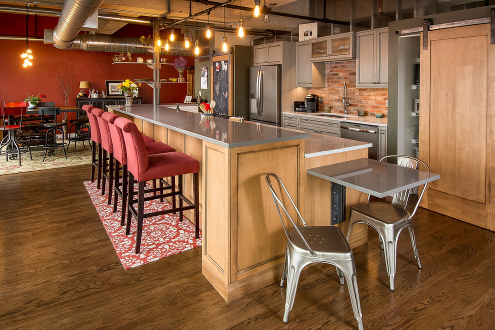 Exempel på ett stort industriellt grå linjärt grått kök med öppen planlösning, med bänkskiva i kvarts, en undermonterad diskho, skåp i shakerstil, grå skåp, rött stänkskydd, stänkskydd i tegel, mellanmörkt trägolv, en köksö och brunt golv