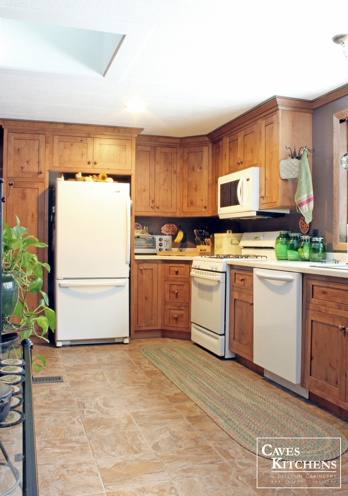 Example of a small mountain style l-shaped laminate floor enclosed kitchen design in New York with a drop-in sink, recessed-panel cabinets, medium tone wood cabinets, solid surface countertops, white appliances and no island