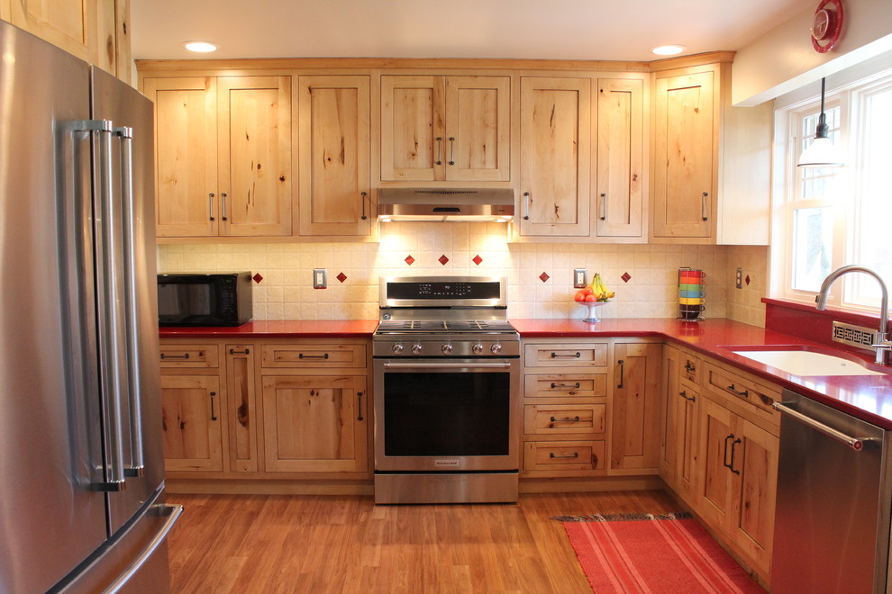 Bild på ett avskilt, mellanstort rustikt l-kök, med en dubbel diskho, skåp i shakerstil, skåp i ljust trä, bänkskiva i kvarts, beige stänkskydd, stänkskydd i keramik, rostfria vitvaror och laminatgolv