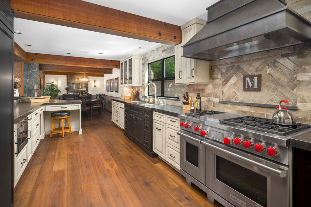 Example of a mid-sized mountain style galley medium tone wood floor eat-in kitchen design in Seattle with a single-bowl sink, raised-panel cabinets, distressed cabinets, granite countertops, gray backsplash, porcelain backsplash and stainless steel appliances