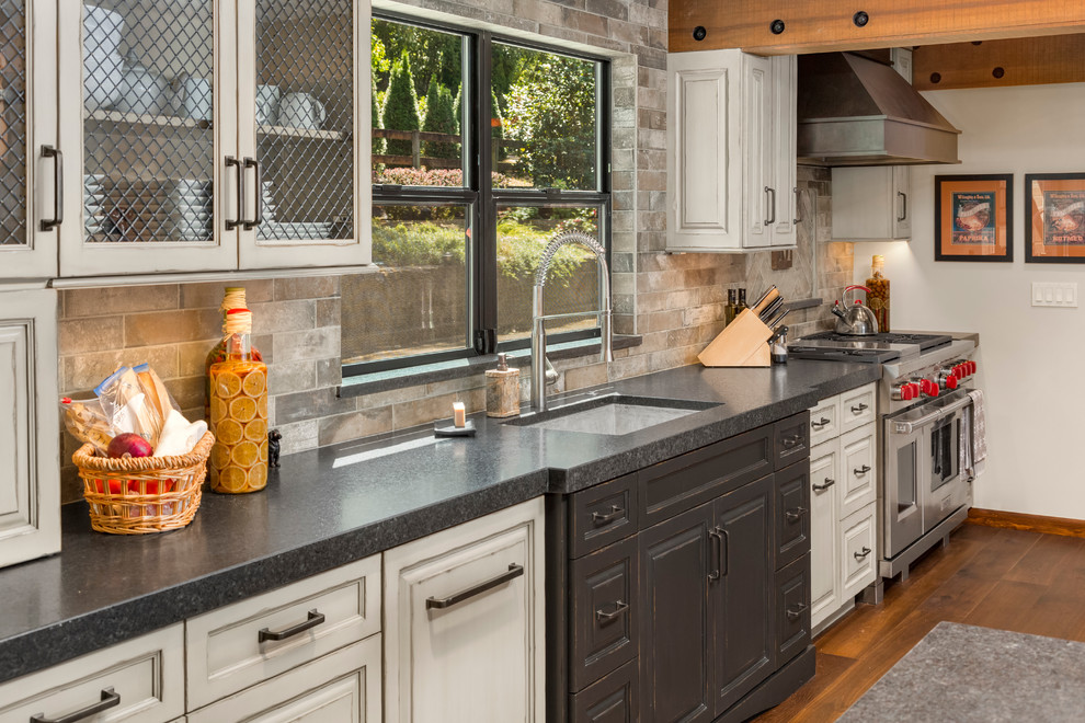 Exempel på ett mellanstort rustikt kök, med en enkel diskho, luckor med upphöjd panel, skåp i slitet trä, granitbänkskiva, grått stänkskydd, stänkskydd i porslinskakel, rostfria vitvaror och mellanmörkt trägolv