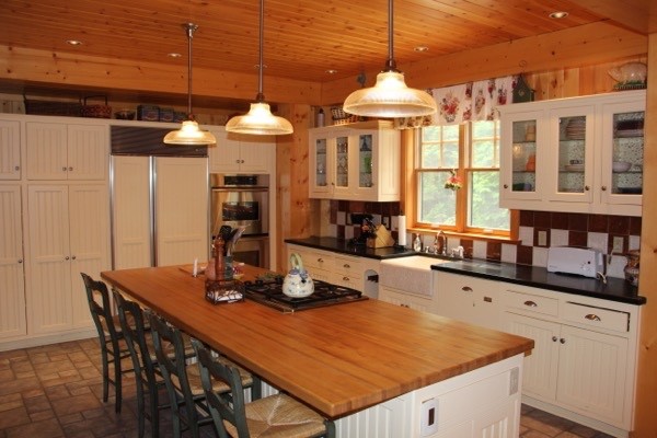 Lantlig inredning av ett mellanstort kök, med en rustik diskho, luckor med glaspanel, vita skåp, träbänkskiva, integrerade vitvaror och en köksö