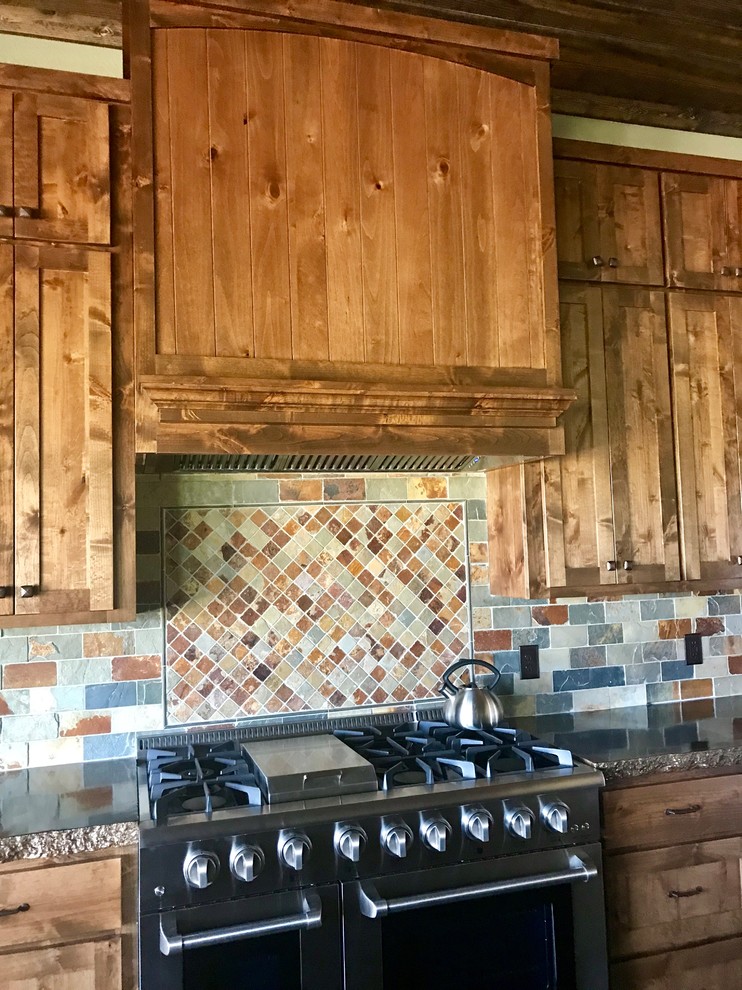 Rustik inredning av ett mellanstort brun brunt kök, med en rustik diskho, skåp i shakerstil, skåp i mörkt trä, bänkskiva i akrylsten, flerfärgad stänkskydd, stänkskydd i skiffer, rostfria vitvaror, betonggolv, en köksö och brunt golv