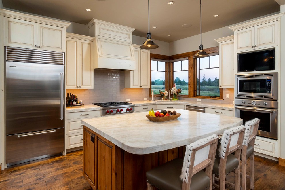 Large mountain style l-shaped dark wood floor and brown floor kitchen photo in Other with an undermount sink, raised-panel cabinets, beige cabinets, gray backsplash, stainless steel appliances, an island, beige countertops and subway tile backsplash