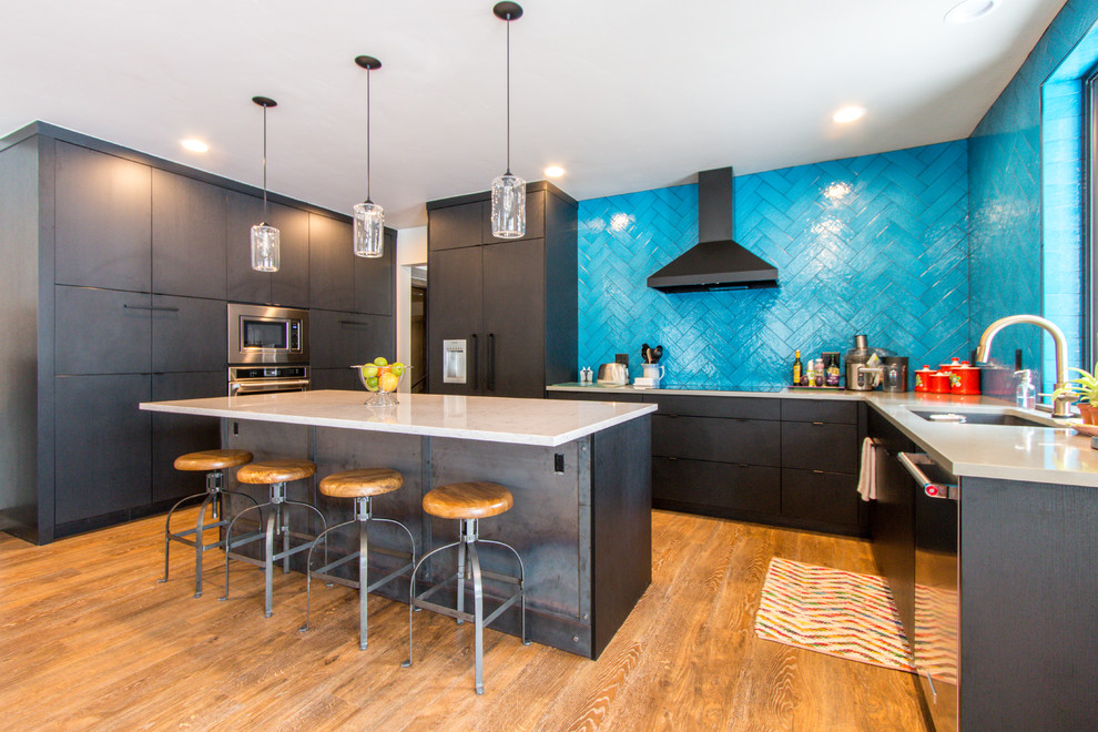 Example of a trendy u-shaped medium tone wood floor and brown floor kitchen design in Dallas with flat-panel cabinets, black cabinets, blue backsplash, ceramic backsplash, an island, an undermount sink, paneled appliances and white countertops