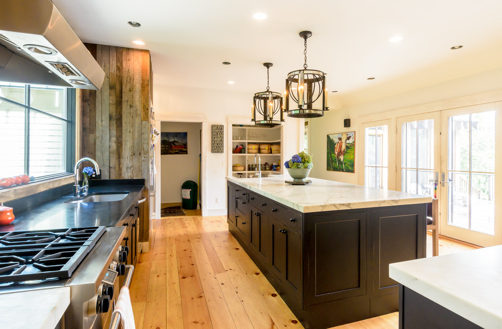 Example of a farmhouse medium tone wood floor eat-in kitchen design in Boston with a farmhouse sink, recessed-panel cabinets, dark wood cabinets, marble countertops, stainless steel appliances and an island