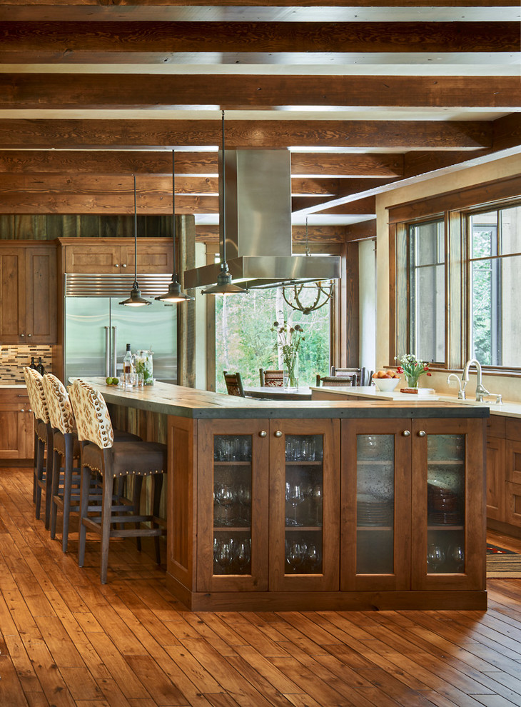 Foto di un cucina con isola centrale rustico con ante di vetro, ante in legno bruno, elettrodomestici in acciaio inossidabile e pavimento in legno massello medio