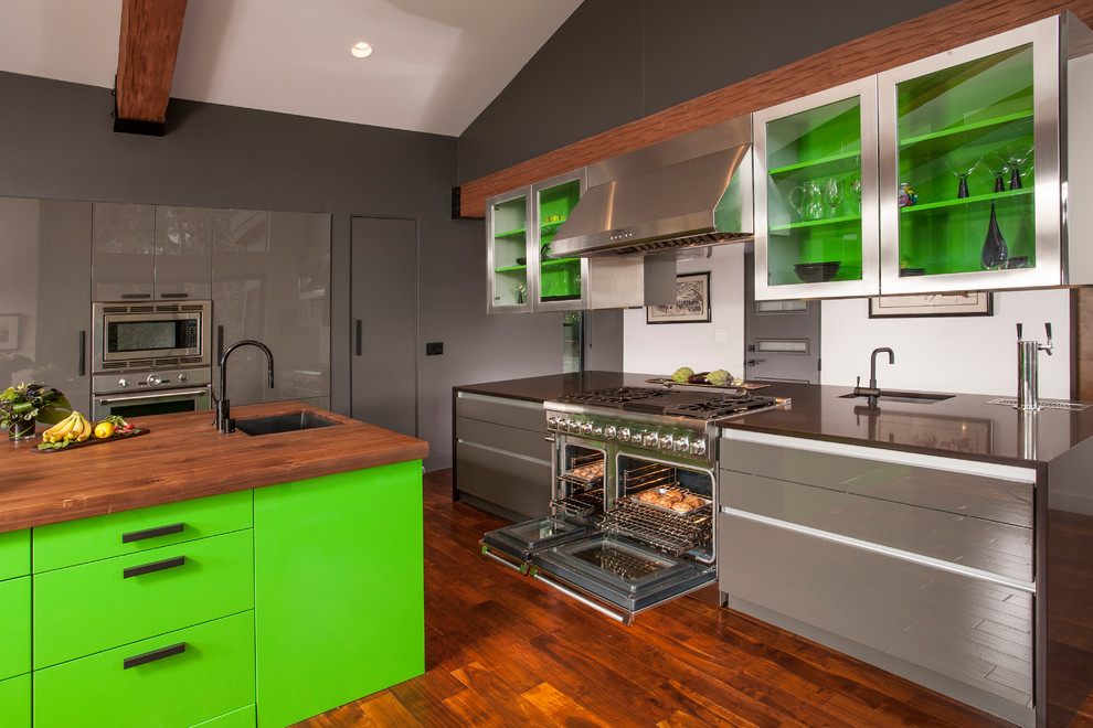 Inredning av ett modernt kök, med en undermonterad diskho, gröna skåp, rostfria vitvaror, mörkt trägolv och en köksö
