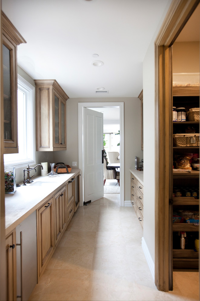 Photo of a large classic galley kitchen pantry in Orange County with a belfast sink, recessed-panel cabinets, distressed cabinets, limestone worktops, beige splashback, stone tiled splashback, integrated appliances, limestone flooring, beige floors and beige worktops.