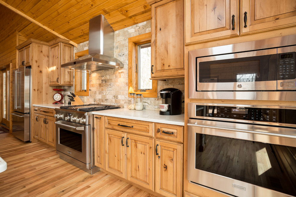 Example of a mountain style light wood floor open concept kitchen design in Milwaukee with an undermount sink, raised-panel cabinets, medium tone wood cabinets, quartzite countertops, stainless steel appliances and an island