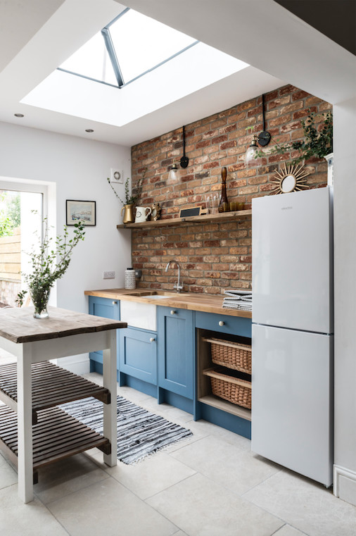 Medium sized industrial single-wall kitchen/diner with a belfast sink, shaker cabinets, blue cabinets, wood worktops, red splashback, brick splashback, stainless steel appliances, cement flooring, an island, grey floors and brown worktops.