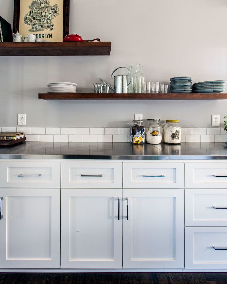 ナッシュビルにあるインダストリアルスタイルのおしゃれなキッチン (一体型シンク、落し込みパネル扉のキャビネット、白いキャビネット、ステンレスカウンター、白いキッチンパネル、サブウェイタイルのキッチンパネル、シルバーの調理設備、濃色無垢フローリング) の写真