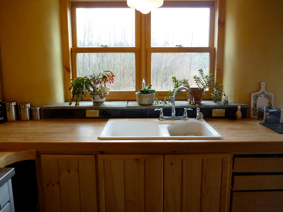 Diseño de cocina rústica con puertas de armario de madera clara, encimera de madera, salpicadero de azulejos de piedra y suelo de pizarra