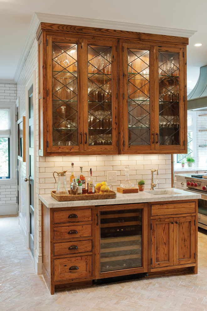 Rustik inredning av ett kök, med en undermonterad diskho, luckor med glaspanel, skåp i mellenmörkt trä, granitbänkskiva, vitt stänkskydd, stänkskydd i tunnelbanekakel och rostfria vitvaror