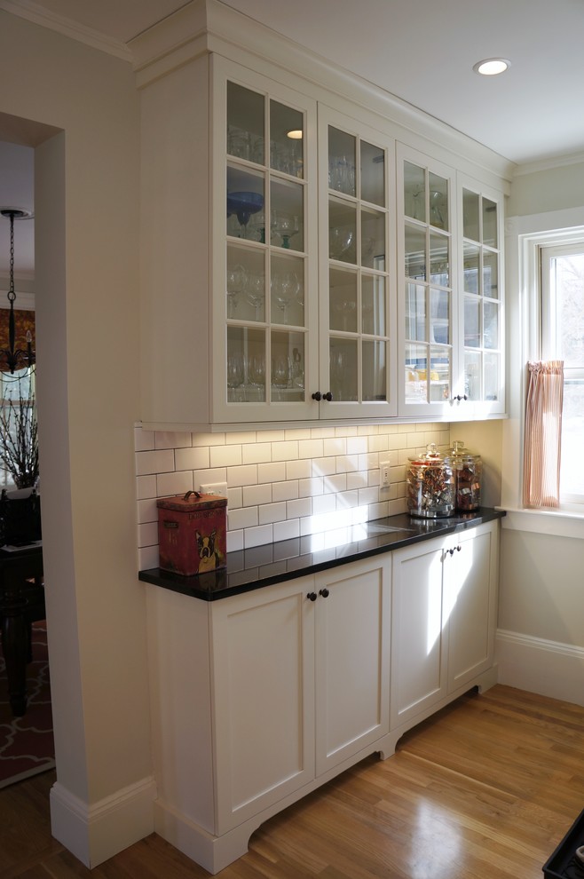 Inredning av ett rustikt avskilt, litet svart svart l-kök, med en undermonterad diskho, luckor med infälld panel, granitbänkskiva, vitt stänkskydd, stänkskydd i tunnelbanekakel, rostfria vitvaror, ljust trägolv, en köksö, vita skåp och beiget golv