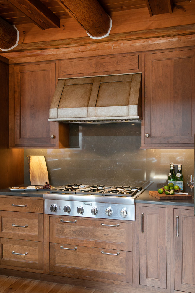 Bild på ett mellanstort rustikt grå grått kök, med luckor med infälld panel, skåp i mellenmörkt trä, bänkskiva i kvarts, grått stänkskydd, stänkskydd i sten, rostfria vitvaror, ljust trägolv och en köksö