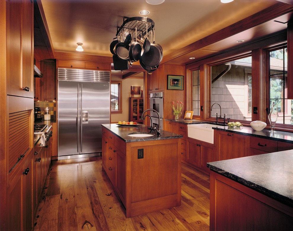 Exemple d'une cuisine craftsman en bois brun fermée avec un évier de ferme, un plan de travail en granite, un électroménager en acier inoxydable, îlot, un placard à porte shaker, un sol en bois brun et fenêtre au-dessus de l'évier.