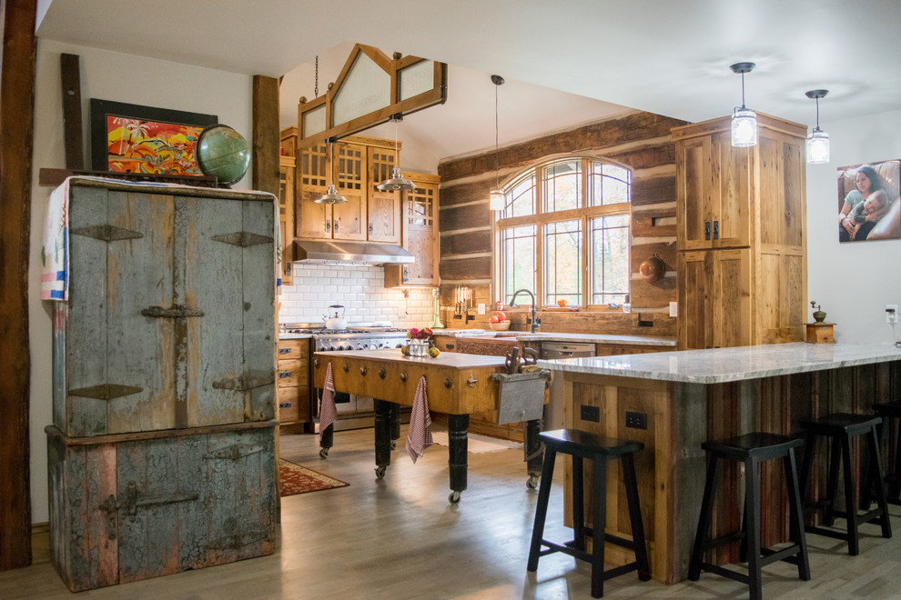 Exempel på ett rustikt grå grått u-kök, med en rustik diskho, skåp i shakerstil, skåp i mellenmörkt trä, vitt stänkskydd, stänkskydd i tunnelbanekakel, rostfria vitvaror, ljust trägolv, en köksö och beiget golv