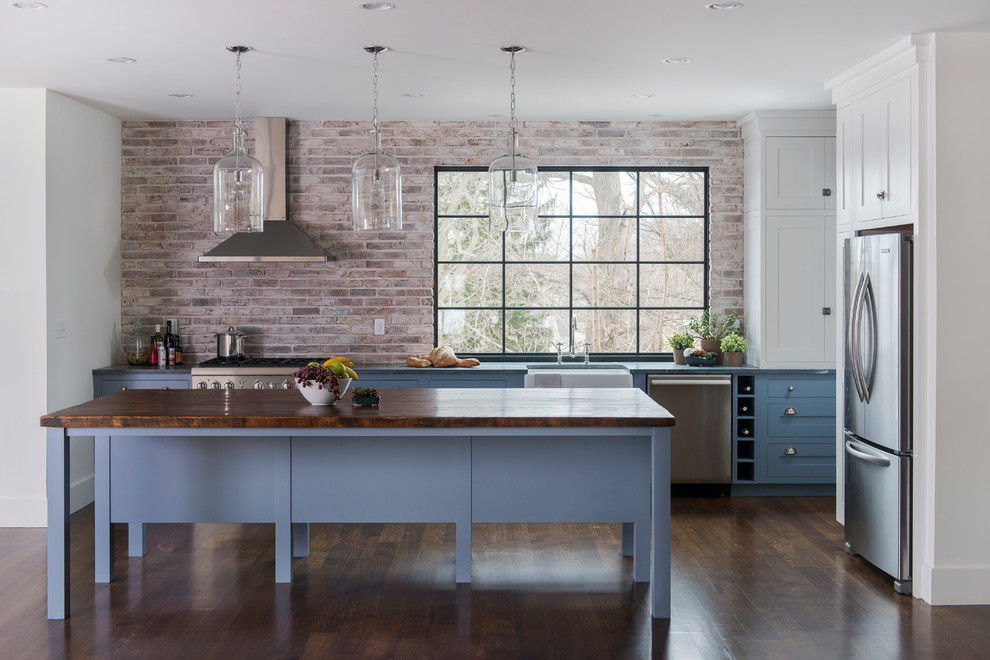 Lantlig inredning av ett mellanstort kök, med en rustik diskho, luckor med infälld panel, blå skåp, träbänkskiva, stänkskydd i tegel, rostfria vitvaror, mörkt trägolv och en köksö
