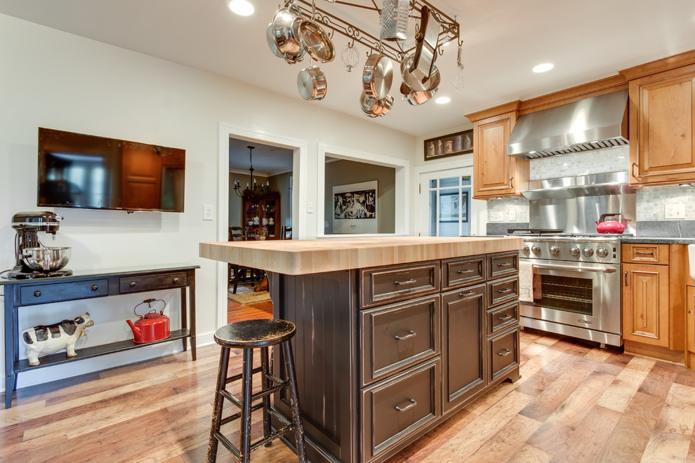 This is an example of a medium sized rustic l-shaped kitchen in Raleigh with raised-panel cabinets, light wood cabinets, wood worktops, stainless steel appliances, medium hardwood flooring, an island and brown floors.