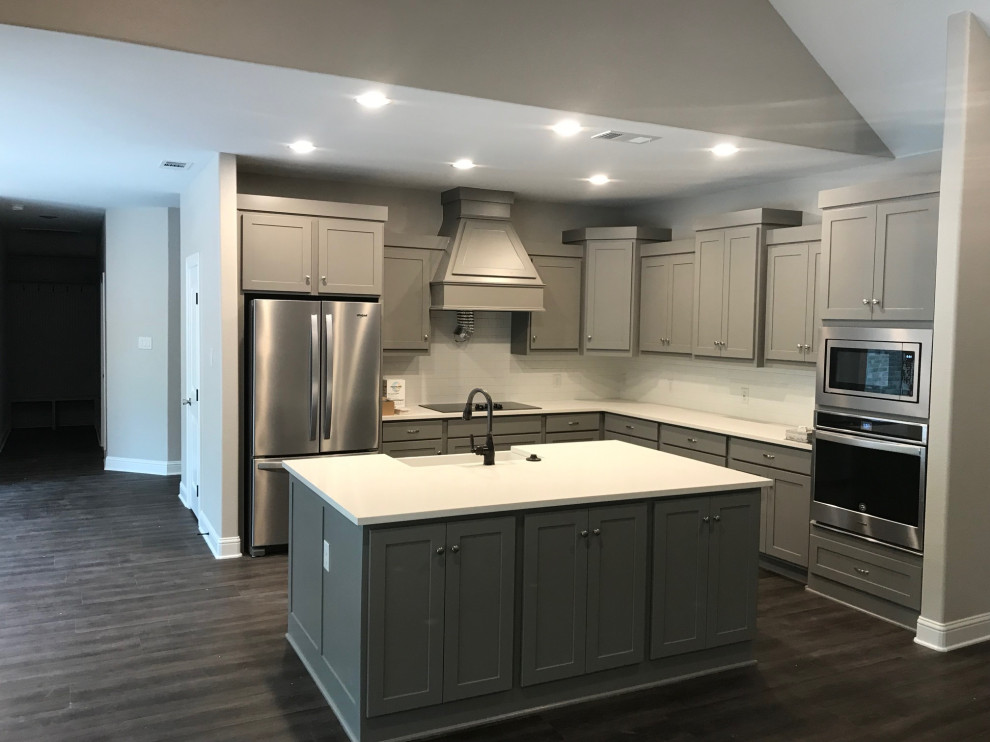 Inspiration for a mid-sized timeless l-shaped medium tone wood floor and brown floor eat-in kitchen remodel in Dallas with a farmhouse sink, recessed-panel cabinets, gray cabinets, quartzite countertops, white backsplash, ceramic backsplash, stainless steel appliances, an island and white countertops