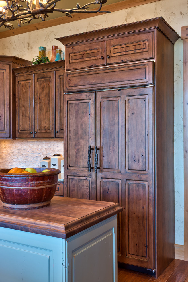 Modelo de cocina rústica con armarios con paneles con relieve, puertas de armario de madera en tonos medios, encimera de madera y electrodomésticos con paneles