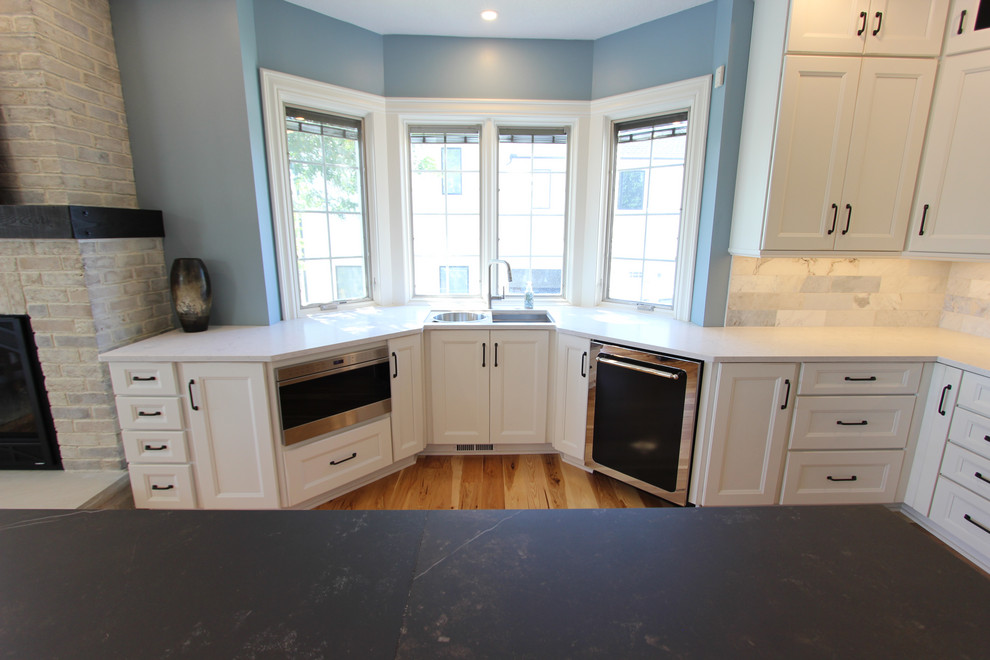 Foto på ett stort rustikt vit kök, med en undermonterad diskho, släta luckor, vita skåp, bänkskiva i kvarts, blått stänkskydd, stänkskydd i marmor, svarta vitvaror, mellanmörkt trägolv och en köksö