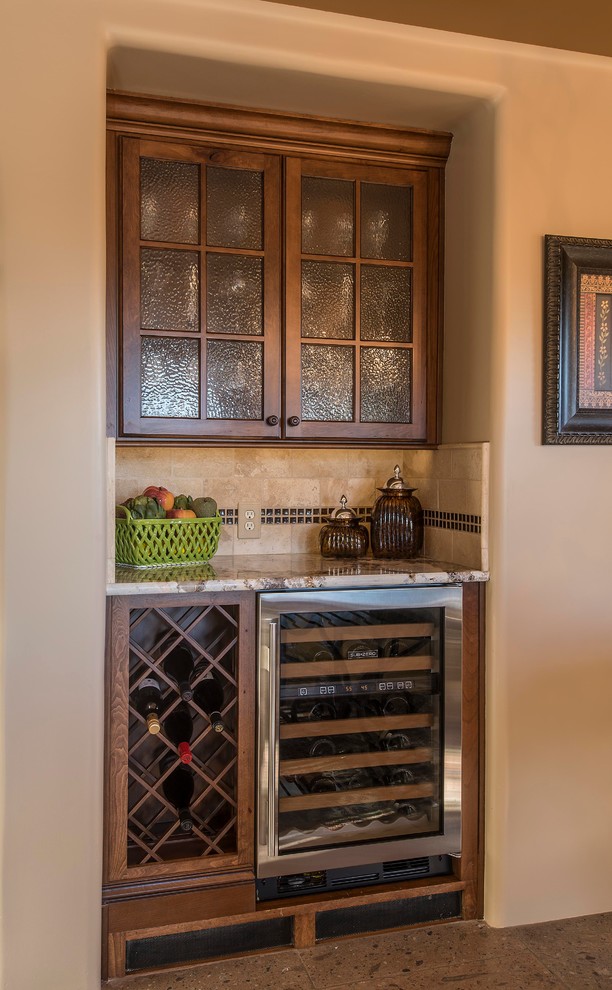 This is an example of an expansive rural l-shaped kitchen/diner in Phoenix with a belfast sink, glass-front cabinets, brown cabinets, granite worktops, beige splashback, stone tiled splashback, stainless steel appliances, brick flooring and an island.