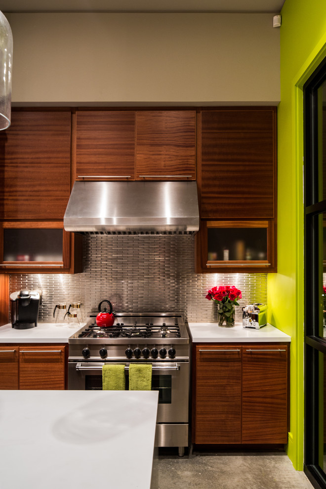 Imagen de cocina comedor minimalista con armarios con paneles lisos, puertas de armario de madera oscura, salpicadero metalizado, electrodomésticos de acero inoxidable, suelo de cemento y una isla