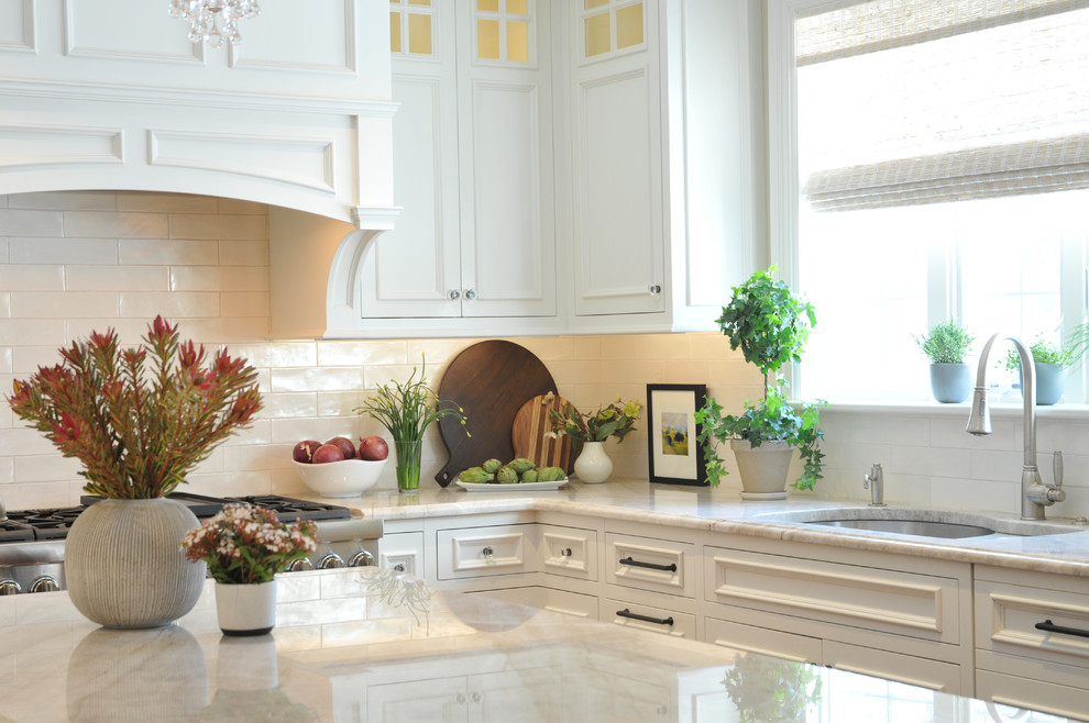 Design ideas for a large traditional u-shaped open plan kitchen in Boston with a submerged sink, recessed-panel cabinets, white cabinets, marble worktops, white splashback, ceramic splashback, integrated appliances, medium hardwood flooring, an island, brown floors and beige worktops.