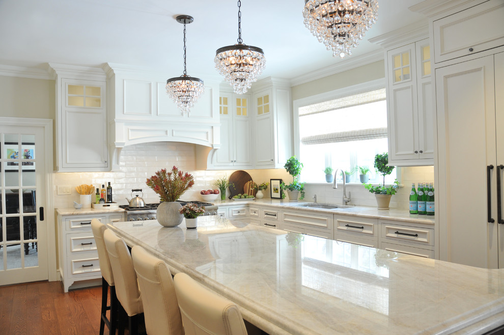 Large traditional l-shaped open plan kitchen in Boston with a submerged sink, recessed-panel cabinets, white cabinets, marble worktops, white splashback, ceramic splashback, integrated appliances, medium hardwood flooring, an island, brown floors and white worktops.