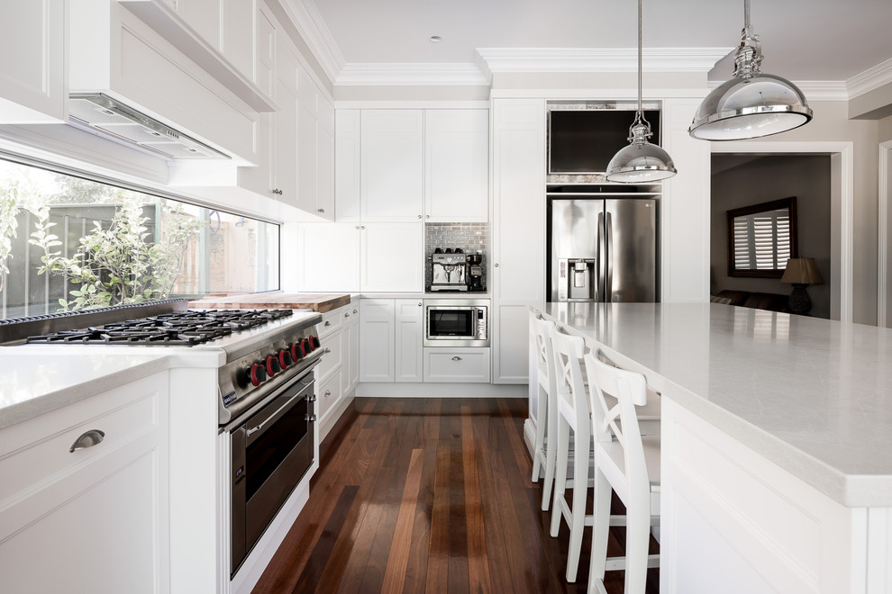 This is an example of a medium sized l-shaped kitchen/diner in Perth with a single-bowl sink, shaker cabinets, white cabinets, engineered stone countertops, white splashback, window splashback, stainless steel appliances, medium hardwood flooring and an island.