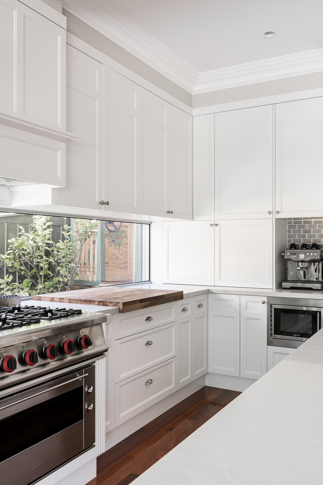 This is an example of a medium sized l-shaped kitchen/diner in Perth with a single-bowl sink, shaker cabinets, white cabinets, engineered stone countertops, white splashback, window splashback, stainless steel appliances, medium hardwood flooring and an island.