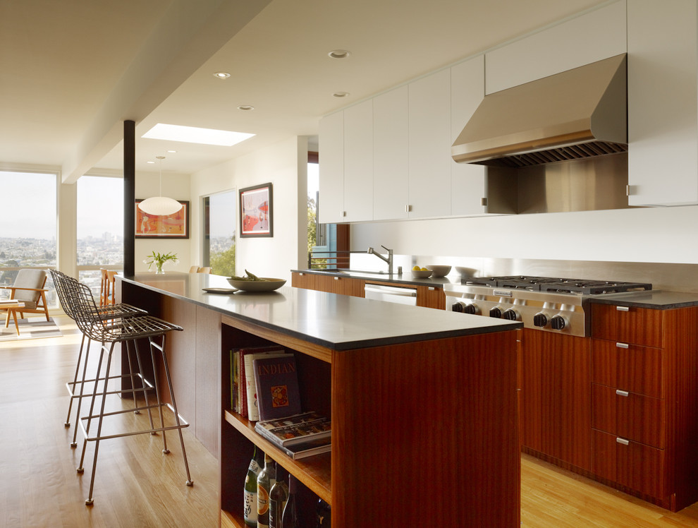 Cette photo montre une cuisine ouverte parallèle moderne en bois brun avec un placard à porte plane, une crédence en dalle métallique et un électroménager en acier inoxydable.