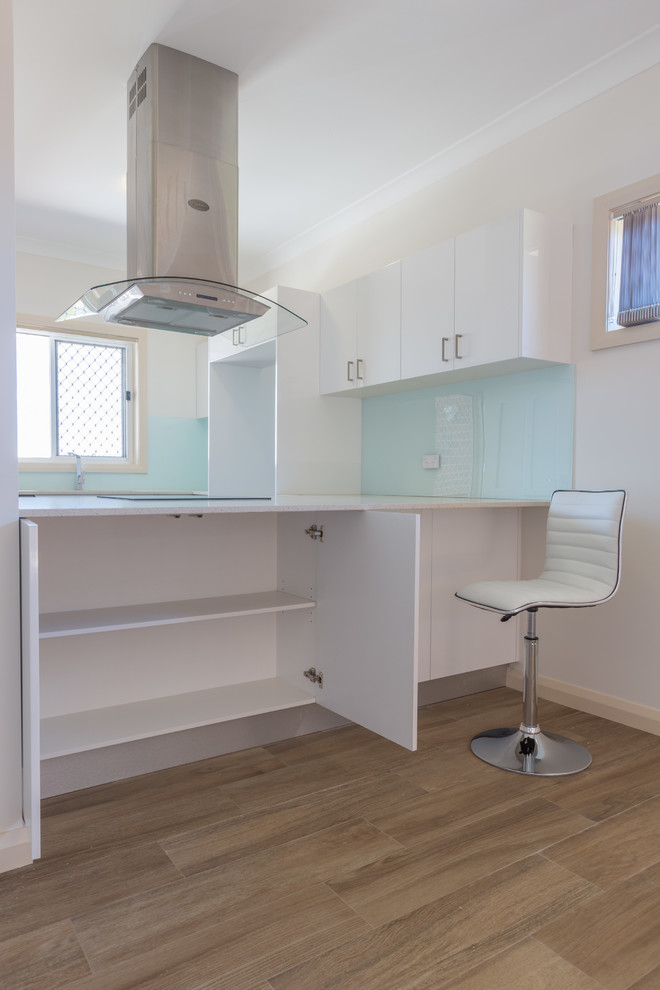 This is an example of a medium sized contemporary u-shaped kitchen/diner in Sydney with a submerged sink, louvered cabinets, white cabinets, engineered stone countertops, green splashback, glass sheet splashback, stainless steel appliances, ceramic flooring and a breakfast bar.