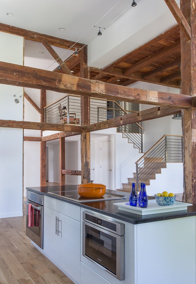 Foto på ett stort funkis linjärt kök med öppen planlösning, med släta luckor, vita skåp, granitbänkskiva, rostfria vitvaror, mellanmörkt trägolv och en köksö