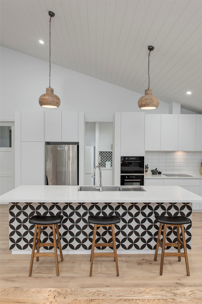 Eat-in kitchen - large contemporary single-wall light wood floor eat-in kitchen idea in Melbourne with a farmhouse sink, flat-panel cabinets, white cabinets, quartz countertops, white backsplash, ceramic backsplash, black appliances and an island