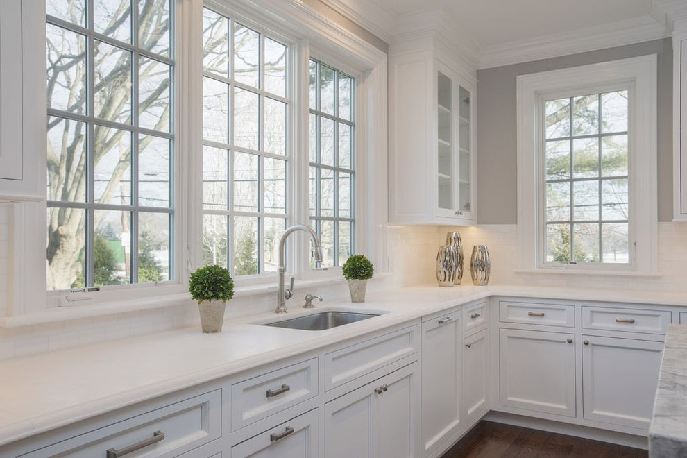 Exempel på ett stort klassiskt grå grått kök, med en undermonterad diskho, luckor med profilerade fronter, vita skåp, marmorbänkskiva, vitt stänkskydd, rostfria vitvaror, mellanmörkt trägolv, en köksö och brunt golv