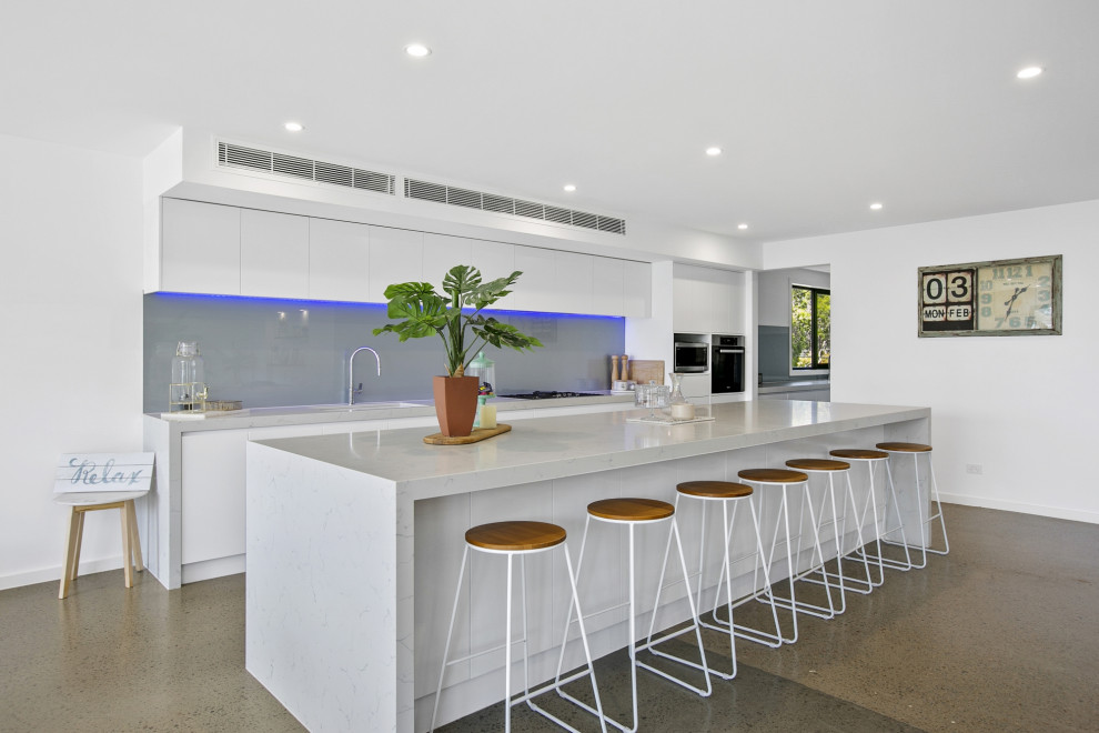 Contemporary galley kitchen in Melbourne with flat-panel cabinets, white cabinets, grey splashback, stainless steel appliances, concrete flooring, an island, grey floors and white worktops.