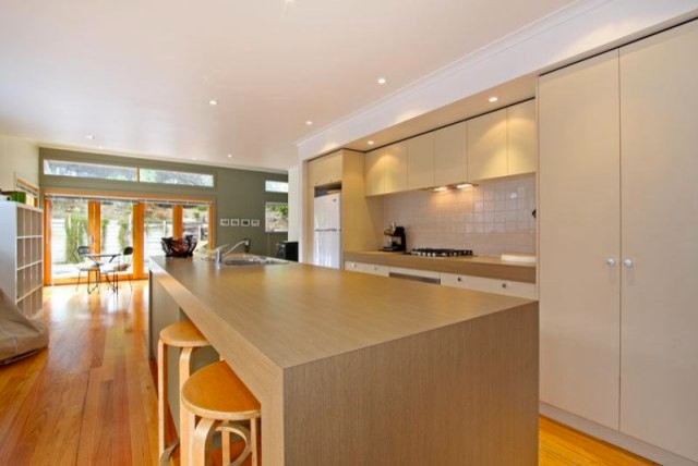 Small beach style galley open plan kitchen in Melbourne with a double-bowl sink, flat-panel cabinets, light wood cabinets, laminate countertops, beige splashback, ceramic splashback, stainless steel appliances, light hardwood flooring and an island.