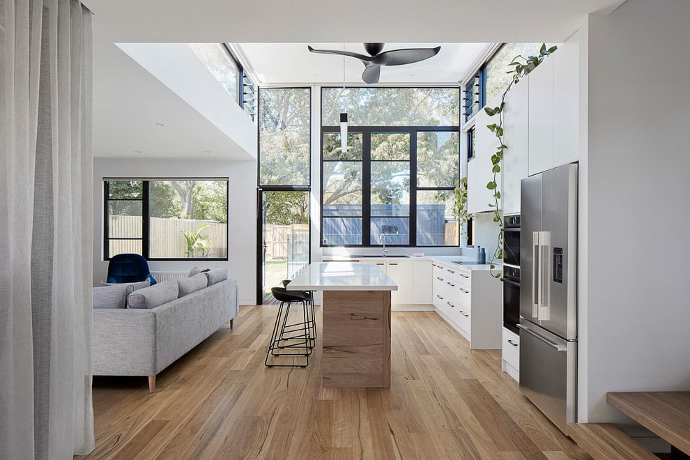 Exempel på ett minimalistiskt vit vitt kök, med släta luckor, vita skåp, rostfria vitvaror, mellanmörkt trägolv, en köksö och brunt golv
