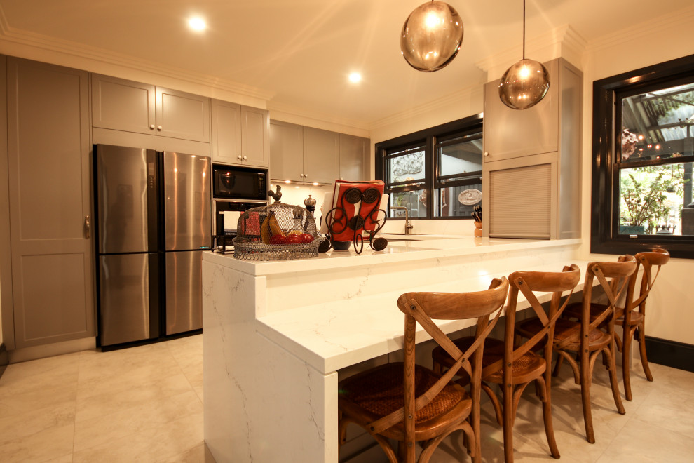 Foto på ett mellanstort funkis vit kök, med en dubbel diskho, skåp i shakerstil, grå skåp, bänkskiva i kvarts, vitt stänkskydd, stänkskydd i sten, svarta vitvaror, klinkergolv i keramik och beiget golv
