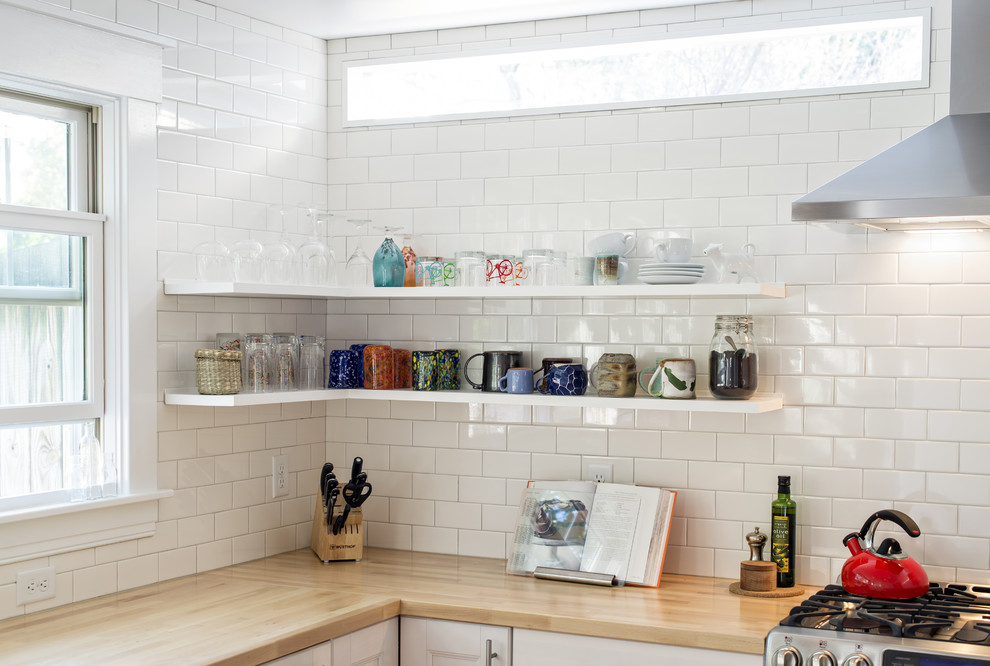 Klassisk inredning av ett avskilt l-kök, med luckor med infälld panel, vita skåp, träbänkskiva, vitt stänkskydd, stänkskydd i tunnelbanekakel och rostfria vitvaror
