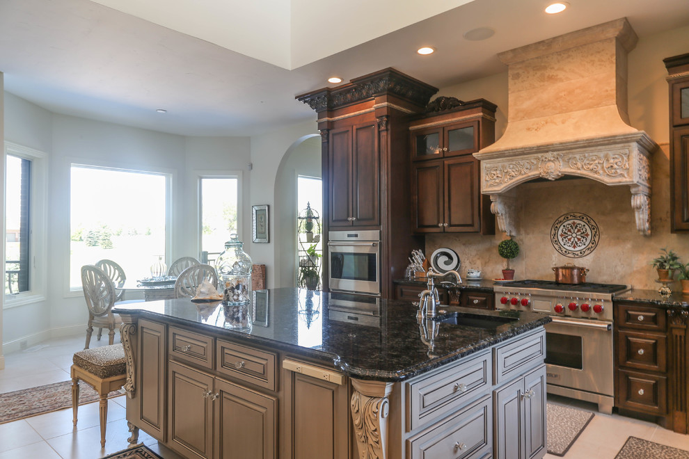 Example of a large tuscan l-shaped porcelain tile and beige floor eat-in kitchen design in Other with an undermount sink, raised-panel cabinets, dark wood cabinets, granite countertops, beige backsplash, stone tile backsplash, stainless steel appliances and two islands